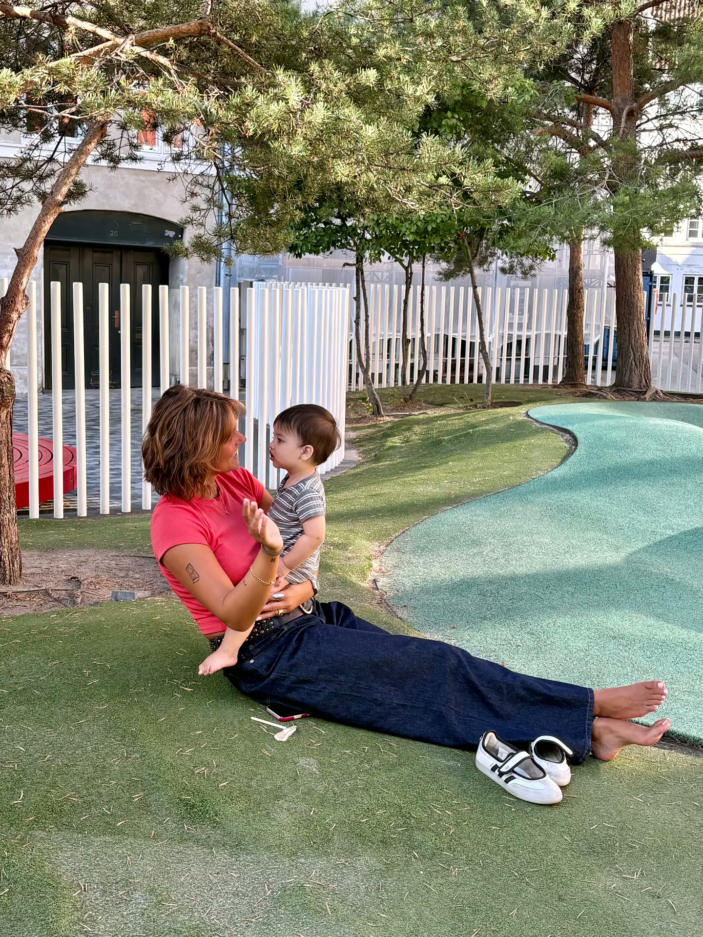 A Nido Care caregiver sitting on the grass with a toddler